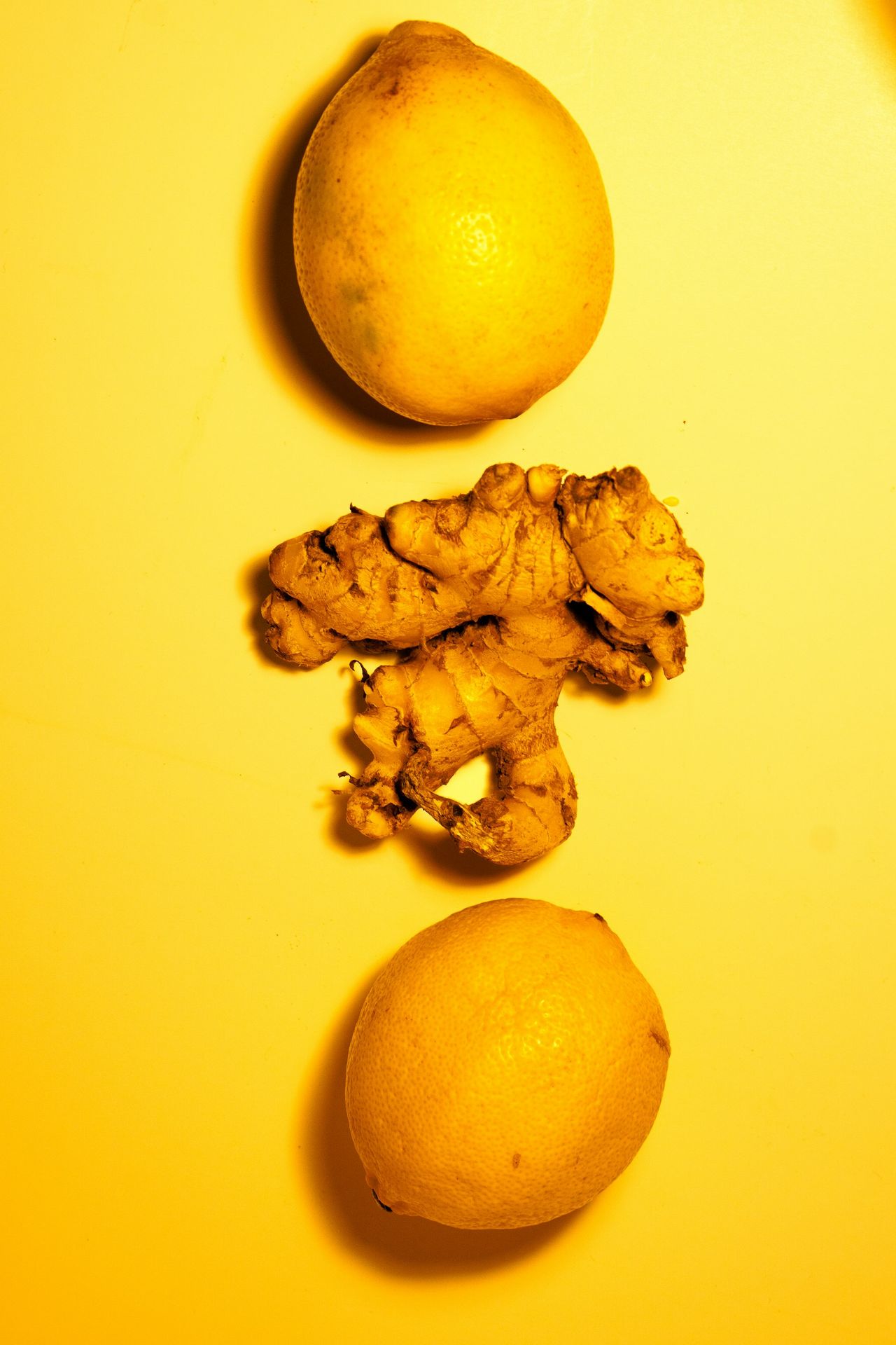 two lemons and a ginger on a yellow surface